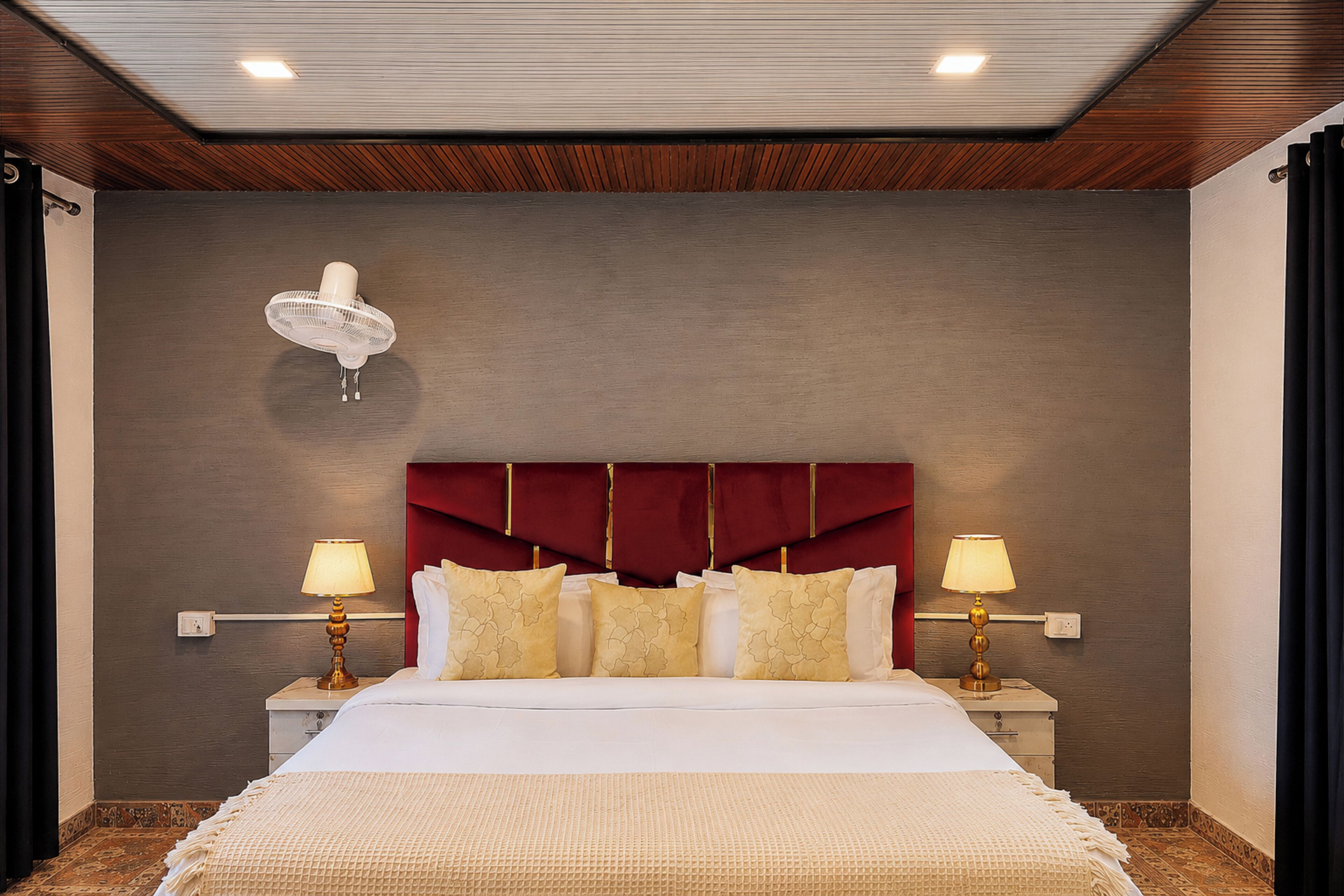 Habitación de hotel con una cama grande, dos lámparas de noche, un cabecero rojo y un ventilador de techo.