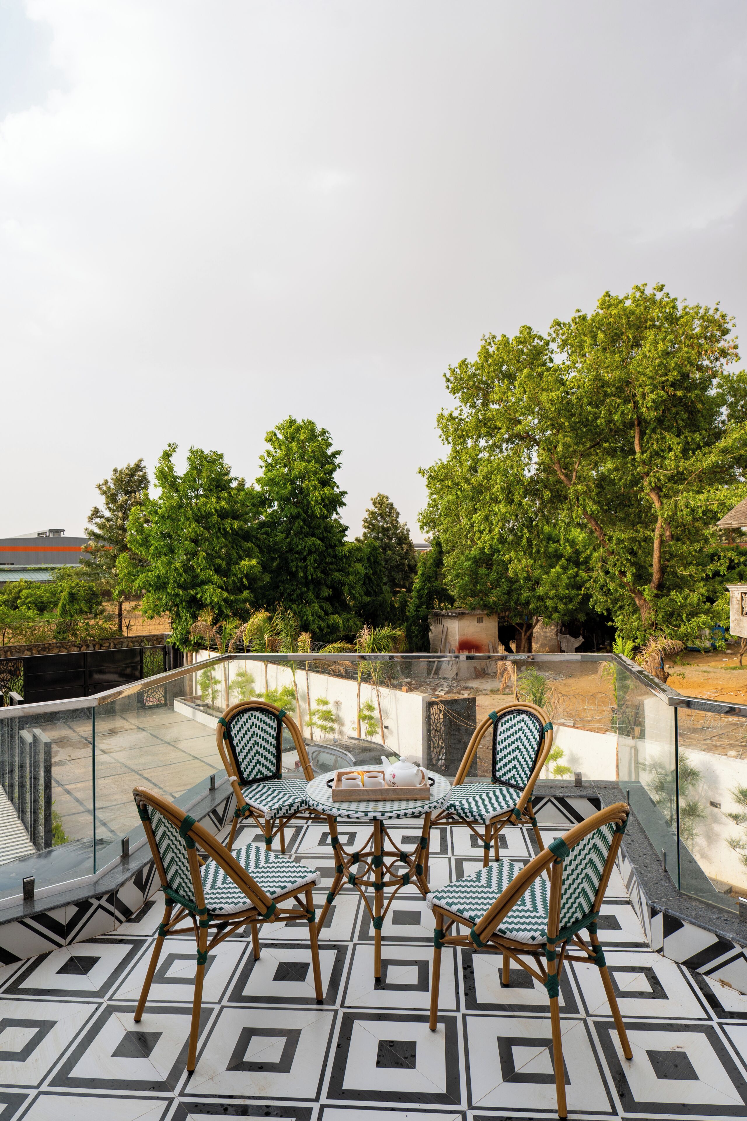 Una terraza en la azotea con barandilla de cristal, suelo estampado y sillas de mimbre.