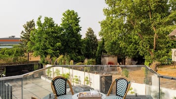 Una terraza en la azotea con barandilla de cristal, suelo estampado y sillas de mimbre.