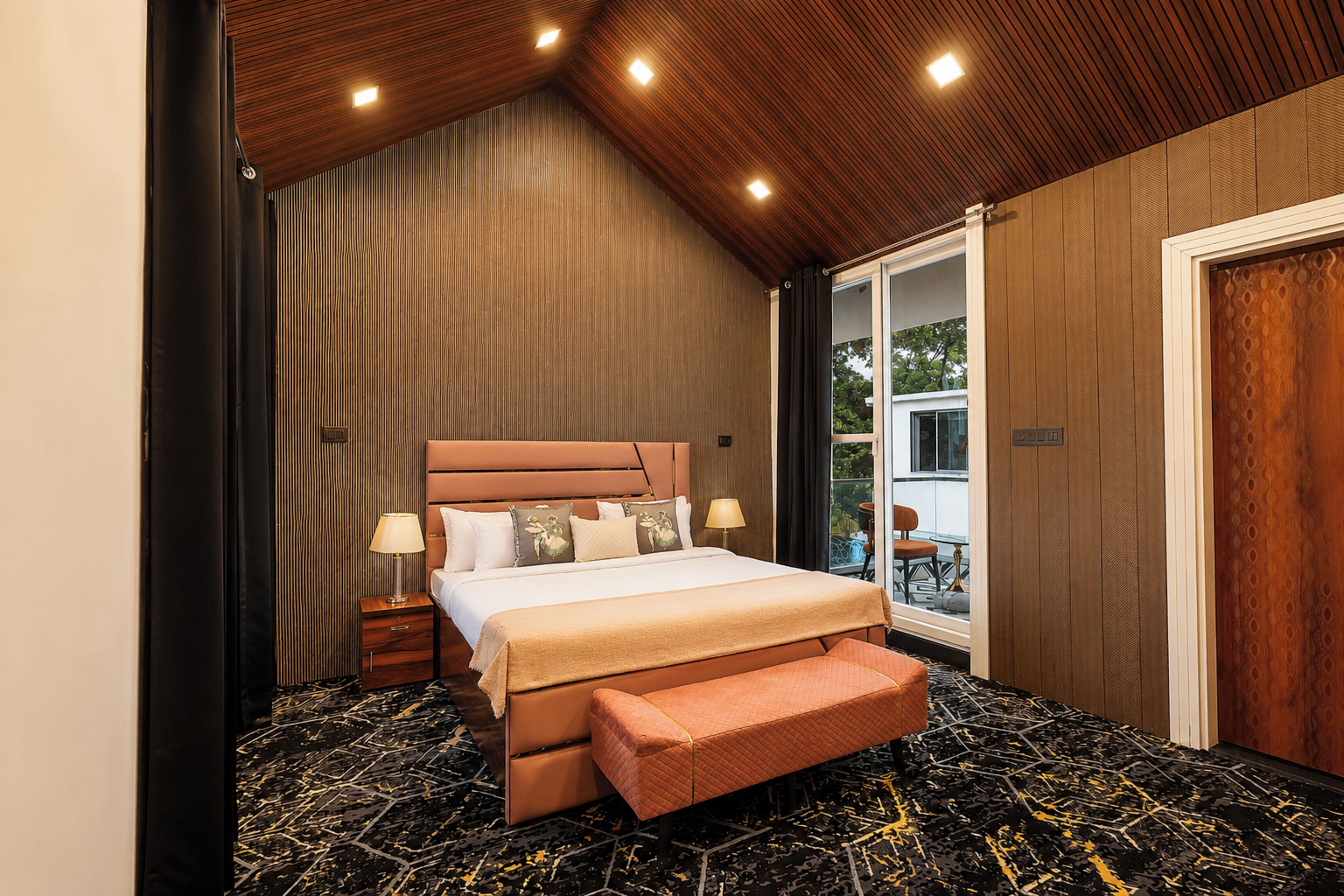 Un dormitorio con cama, mesitas de noche, un banco y vistas al exterior.
