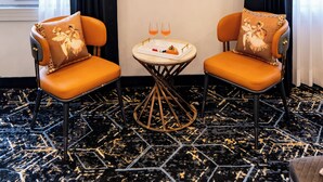 A hotel room with two orange chairs, a small round table with a glass of orange drink, and an air conditioning unit on the wall. - ELIVAAS Signature Raj Farms | 3 BHK Villa with Pvt Pool (Gurugram)