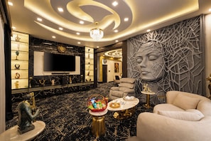 A modern living room with a marble floor, a chandelier, a sofa, a television, and a decorative wall. - ELIVAAS Signature Raj Farms | 3 BHK Villa with Pvt Pool (Gurugram)