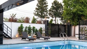 A swimming pool with lounge chairs and a staircase leading to an upper level. - ELIVAAS Signature Raj Farms | 3 BHK Villa with Pvt Pool (Gurugram)