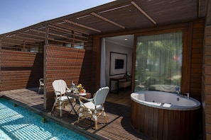 A modern outdoor deck with a hot tub, seating area, and a view of the pool.