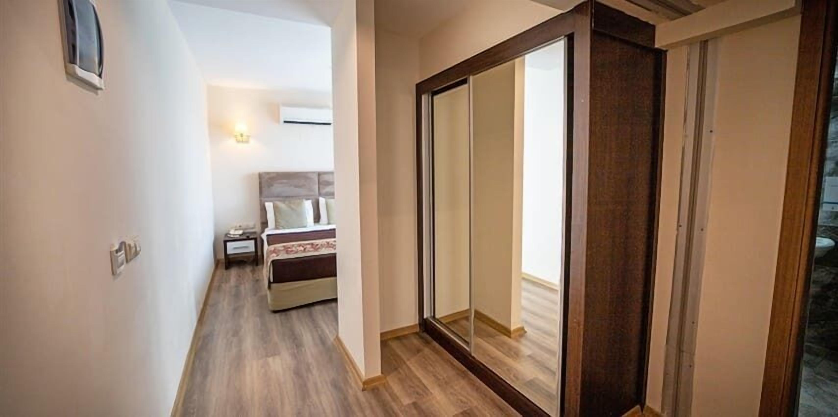 A narrow hallway with a bed and nightstand in the background, a sliding door, and a wall-mounted light fixture.