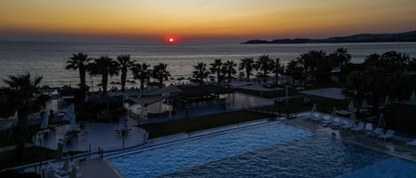 A pool area with lounge chairs and umbrellas, overlooking a body of water at sunset.