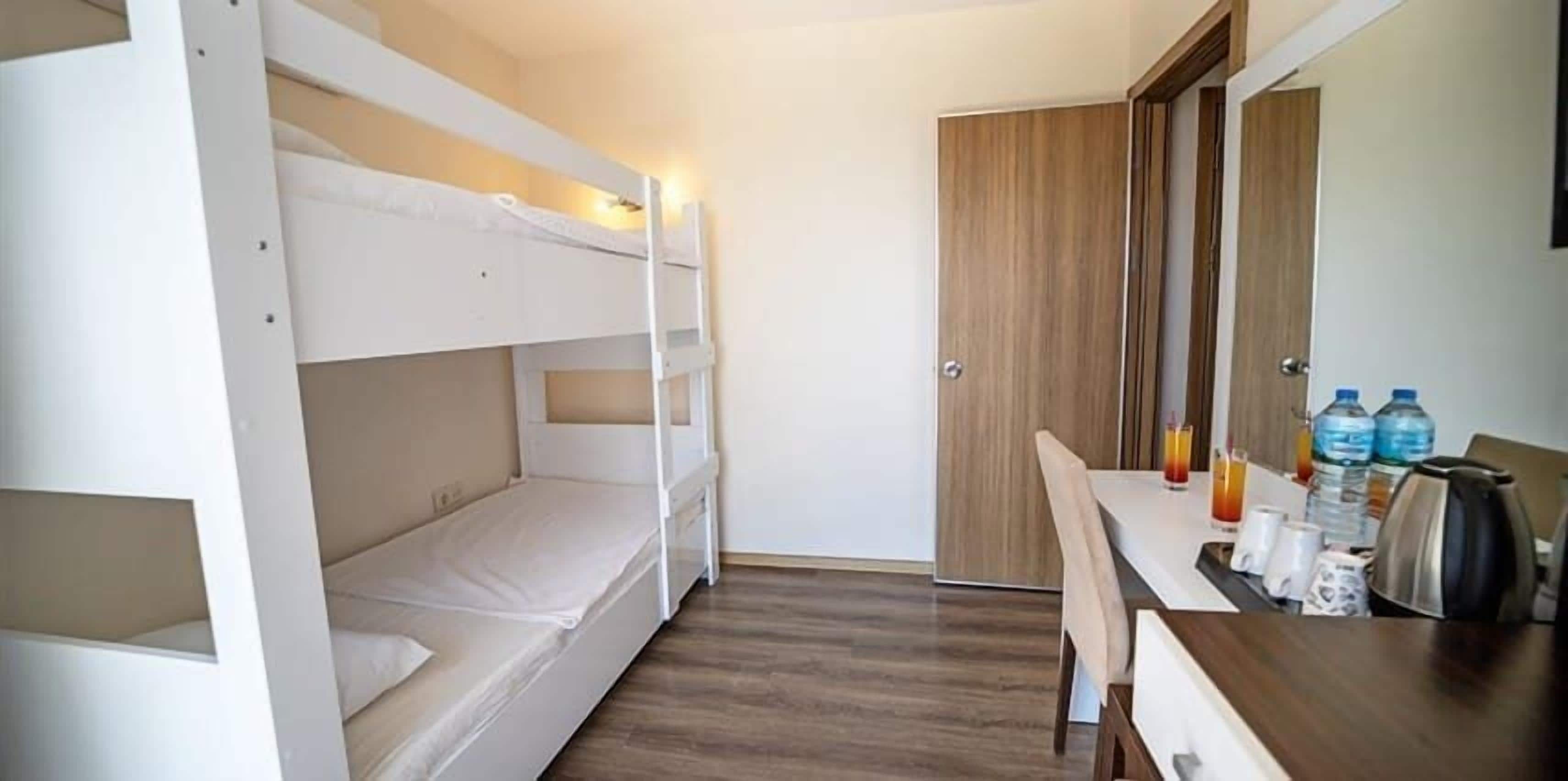 A bunk bed room with a wooden door, a table with a chair, and a mirror.