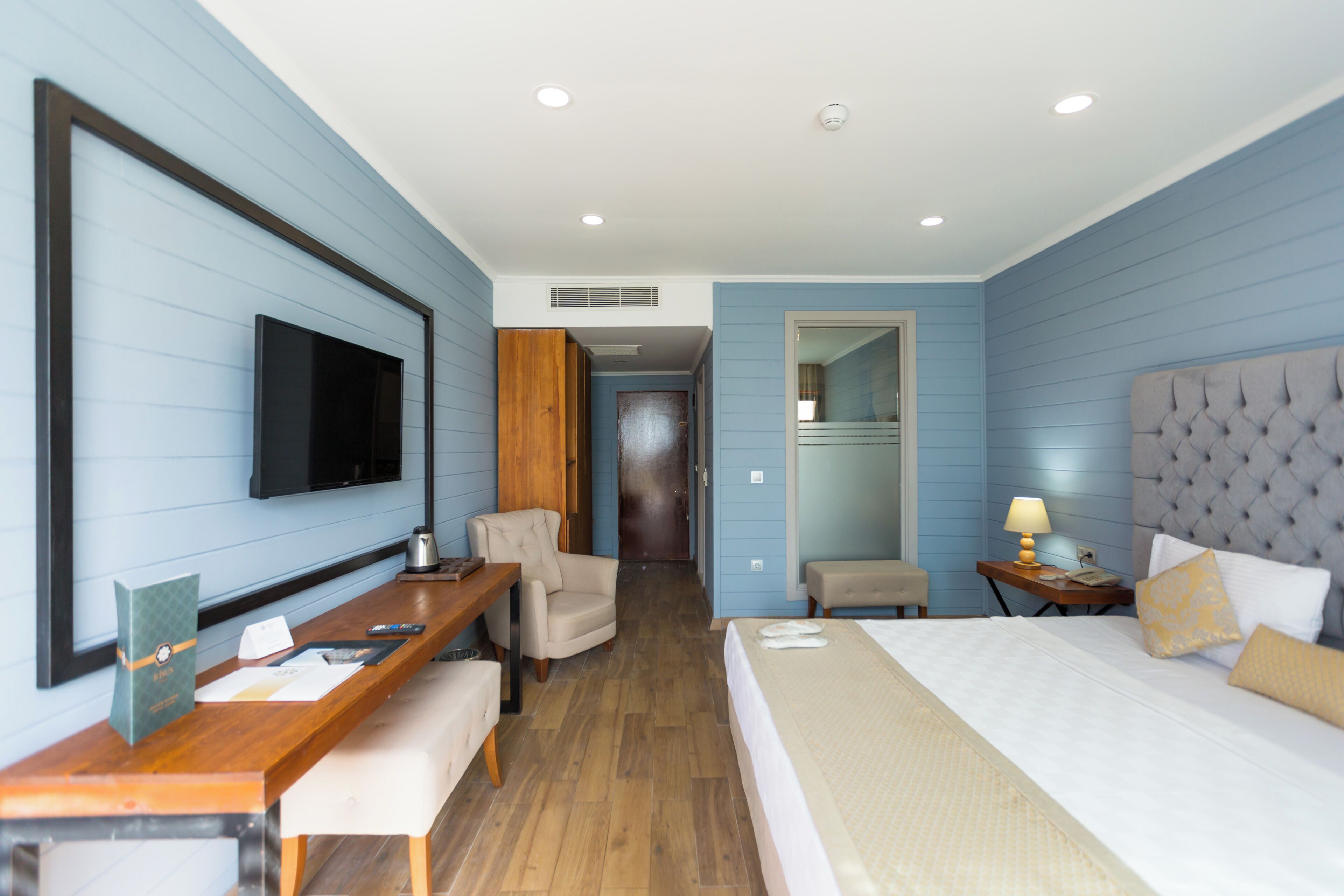 Habitación de hotel con cama, escritorio, silla, televisor y espejo.