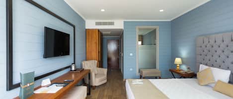 Habitación de hotel con cama, escritorio, silla, televisor y espejo.