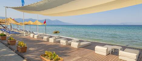 A wooden deck with lounge chairs and planters, overlooking a calm sea with mountains in the distance.