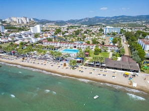 Uma estância costeira com praia, piscina e um hotel com vários andares.