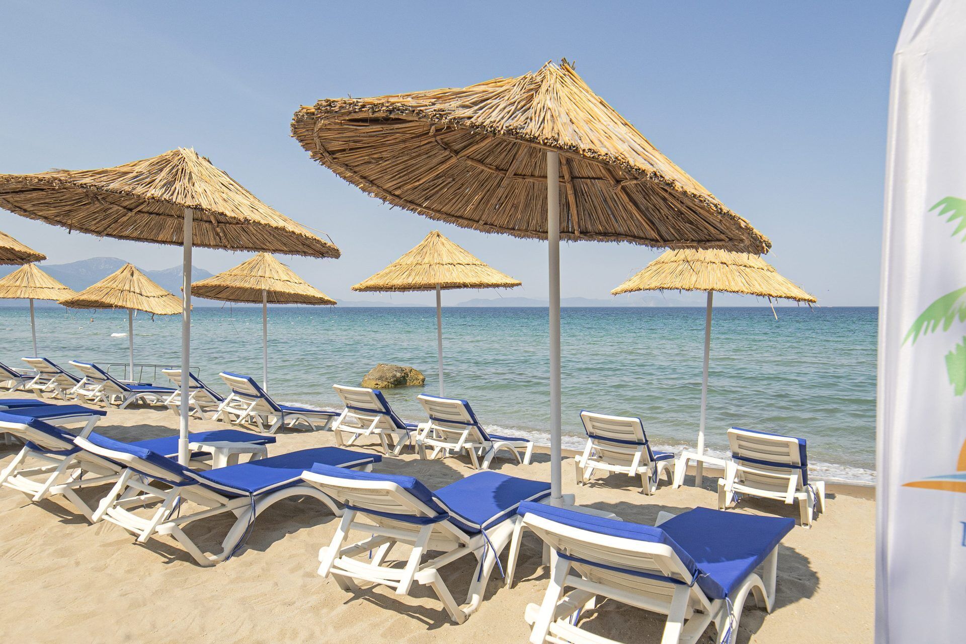 Μια παραλία με σειρές από ξαπλώστρες και ομπρέλες με καλάμια.