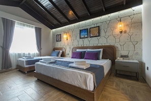 A bedroom with two beds, wooden flooring, stone wall, and a nightstand.