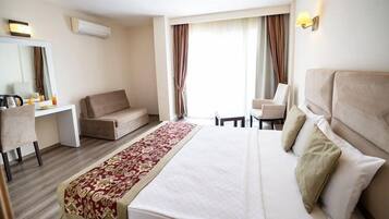 A hotel room with a bed, a desk, a chair, a sofa, a long red and white patterned runner, and a large window with curtains.