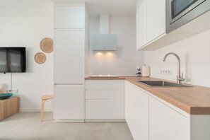 Eine moderne Küche mit weißen Schränken, einer Holz Arbeitsplatte, einer eingebauten Mikrowelle und einem an der Wand montierten Fernseher.
