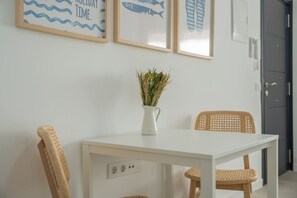 Ein weißer Tisch mit einer Vase gefüllt mit getrockneten Pflanzen, zwei Korbstühle und Wandbilder mit Fischen und Wellen.