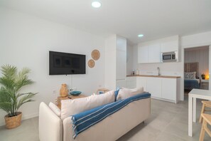 Ein modernes Wohnzimmer mit einer Couch, einem Flachbildfernseher, einer Küchenzeile mit Schränken und einer Mikrowelle sowie einem Esstisch.