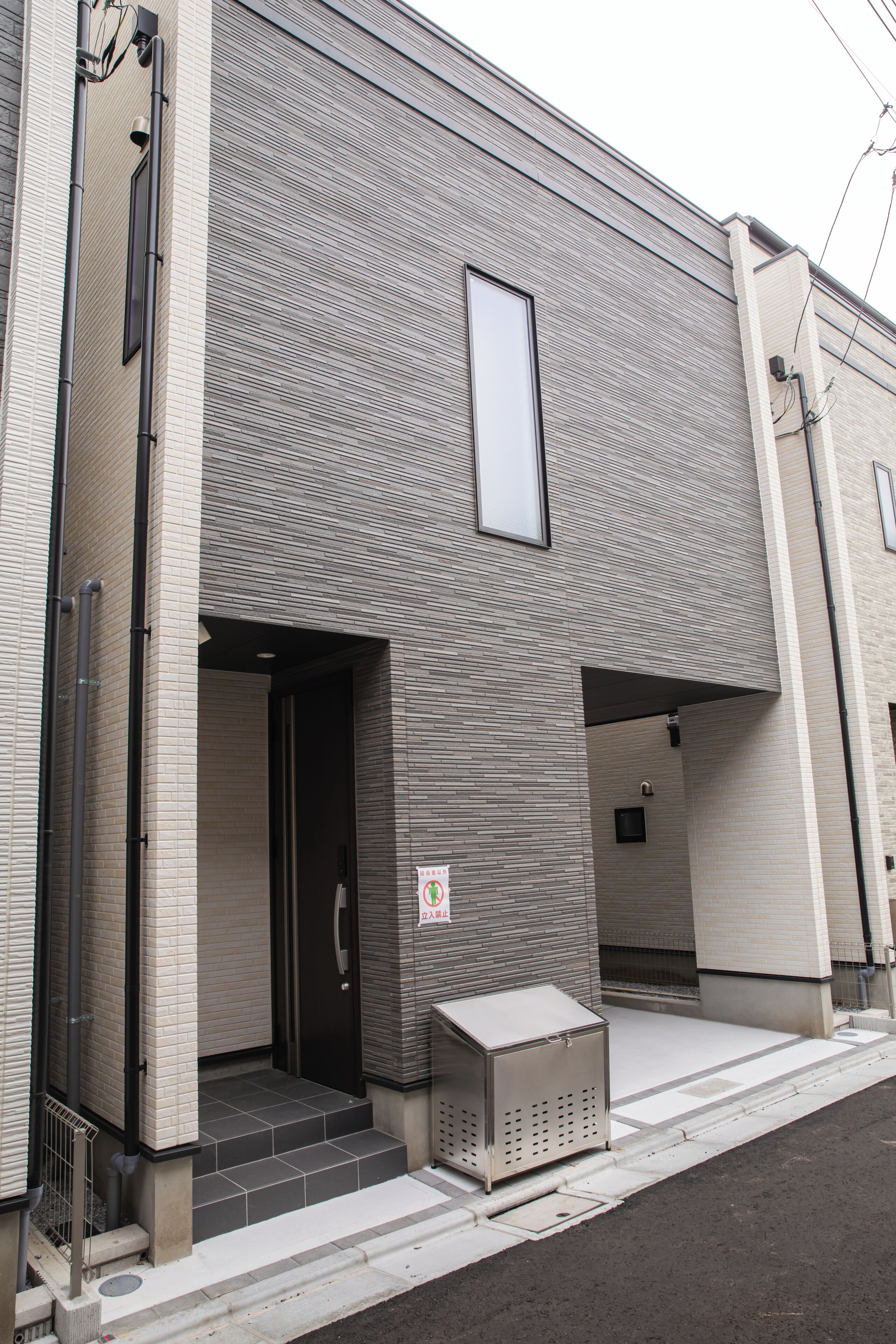 A building with a tiled entrance, a small trash bin, and a visible door.