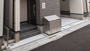 Un bâtiment avec un porche carrelé, une petite poubelle et une porte bien visible.