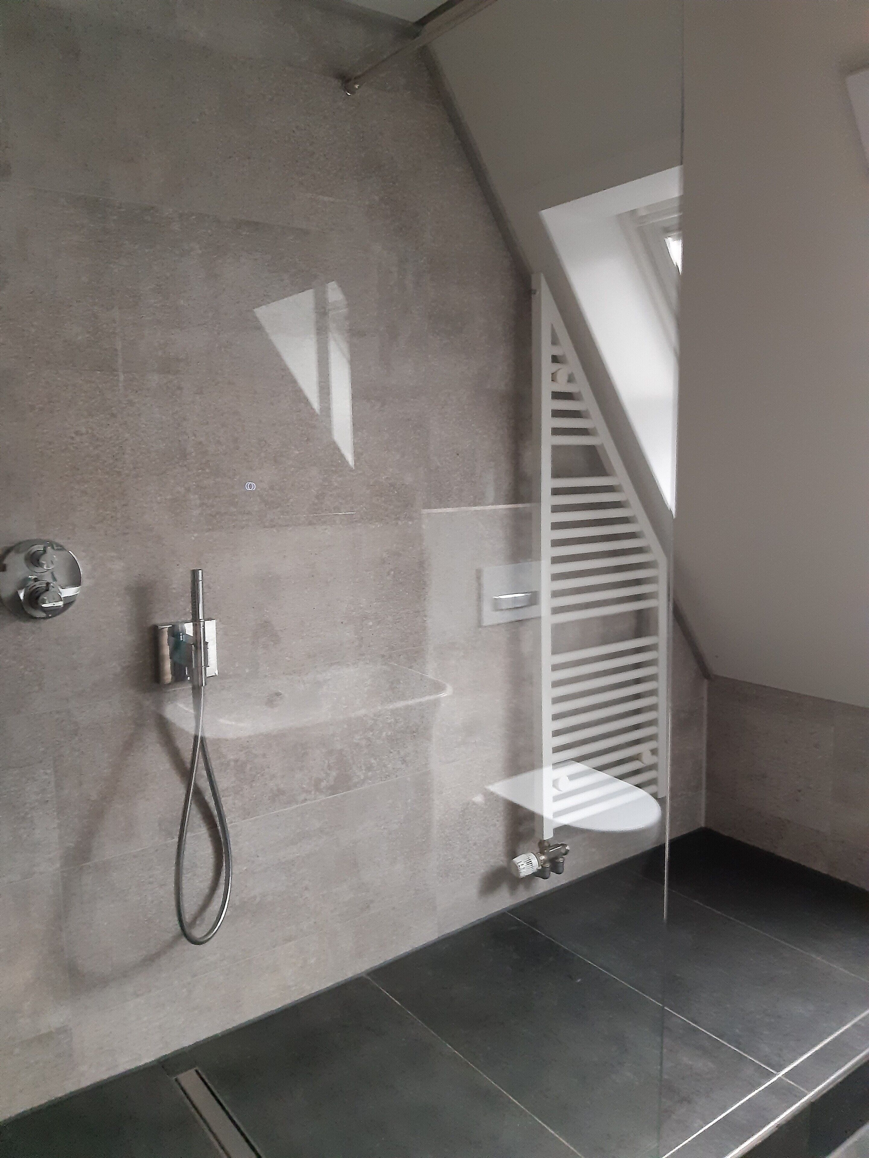 A modern bathroom with a shower, a towel rack, and a glass-enclosed corner.