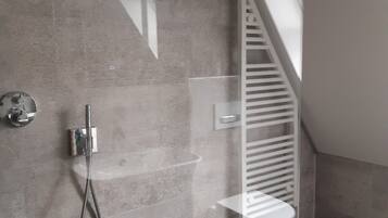A modern bathroom with a shower, a towel rack, and a glass-enclosed corner.