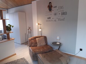 Uma sala de estar moderna com sofá de couro, uma mesinha redonda com abajur, planta pendente e um guarda-roupa.