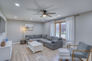 Een moderne woonkamer met een modulaire bank, een witte salontafel, een grijze fauteuil en een plafondventilator.