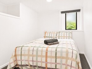 Un dormitorio con cama, ventana con vista a la vegetación y una lámpara en el techo.