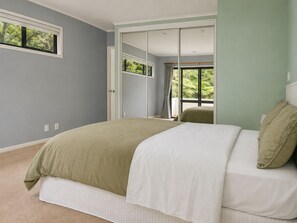 Een slaapkamer met een bed, een raam en een deur naar een andere kamer.