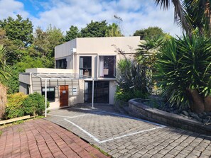 Une maison moderne à deux étages, dotée d’un toit plat, de grandes fenêtres et d’une allée pavée.