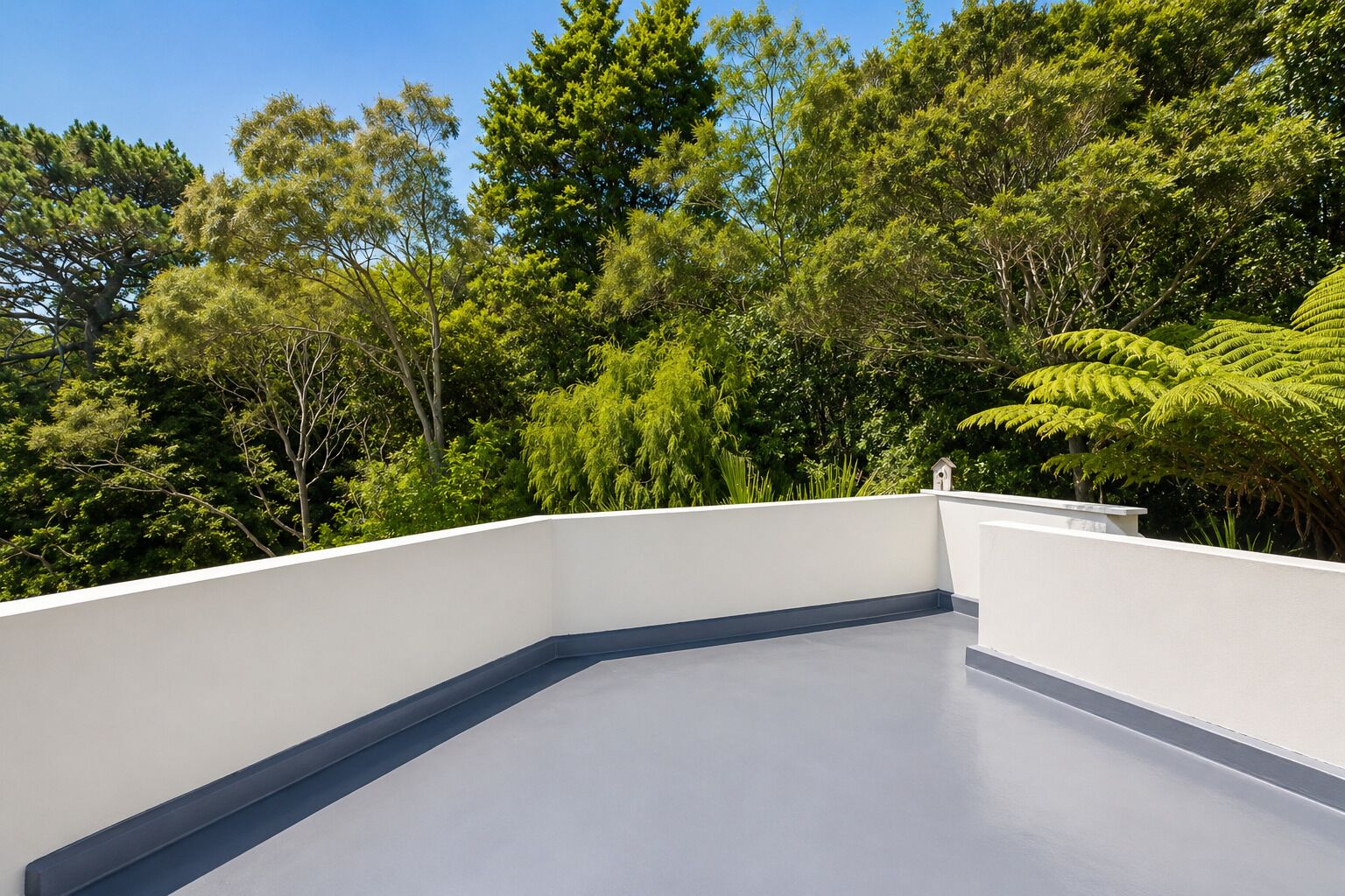 Terraço no telhado com guarda-corrimão branco, cercado por vegetação densa e verde.