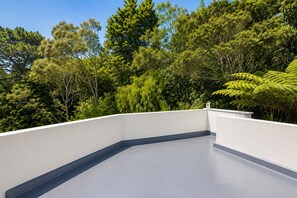 Een terras op het dak met een witte reling, omgeven door weelderige groene beplanting.