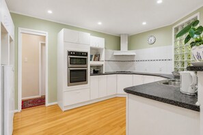 Een moderne keuken met witte kastjes, een dubbele oven, een granieten aanrechtblad en een klok aan de muur.