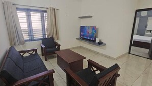 Un soggiorno con divano, poltrone, tavolino, televisione e un letto con specchio.