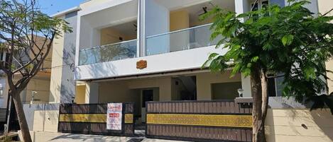 A modern two-story building with a balcony, a gated entrance, and a signboard.