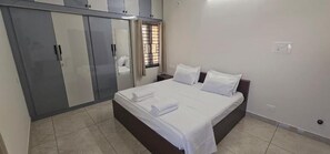Un dormitorio con cama, armario, mesita de noche y ventana con cortinas.