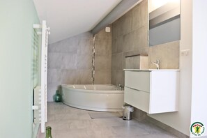Een moderne badkamer met een vrijstaand bad, een wastafel met spiegel en een betegelde vloer.