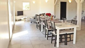 Un espace repas avec une longue table, des chaises et un téléviseur en arrière-plan.