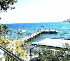A pier extending into calm blue waters, a boat docked at the end, and a building with a blue roof in the foreground.