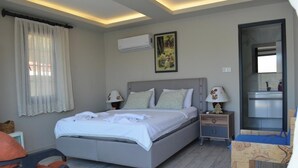 Quarto com cama, mesas de cabeceira, ar condicionado, um quadro e um espelho de banheiro.