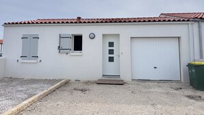 En envåningsbyggnad med en vit fasad, ett rött tegeltak, en ytterdörr, ett litet fönster och en stor garageport.