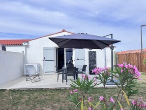 Eine Terrasse mit Tisch, Stühlen und einem großen Sonnenschirm, sowie eine Person, die an der Tür steht.