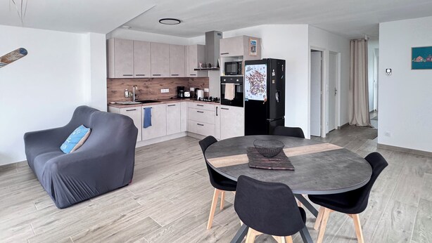 Ett modernt kök med matplats, ett svart kylskåp och en grå soffa.