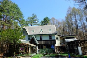 A two-story building with a sloped roof, a porch, and a small garden area. - HAJIMARINOYADO D'LL (Tsumagoi)