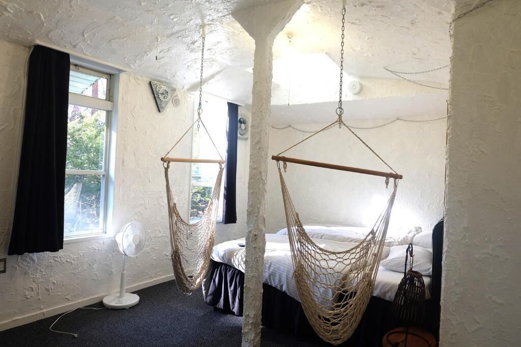 A room with a bed, a fan, and two hammocks.