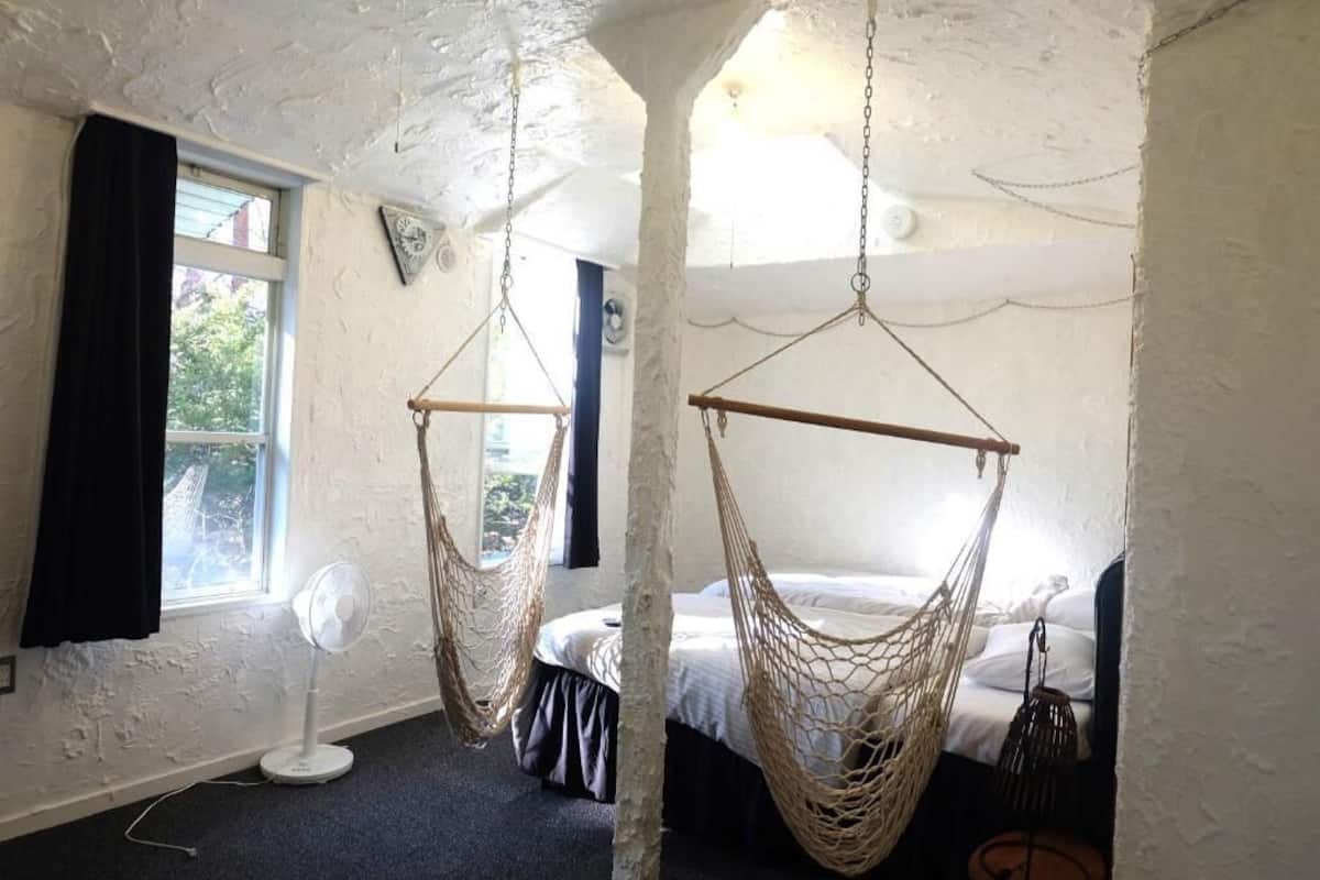 A room with a bed, a fan, and two hammocks.