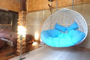 Ein Zimmer mit einem hängenden, blauen Sitzsack, einem Bett mit brauner Bettwäsche und einer Holzbalkendecke.