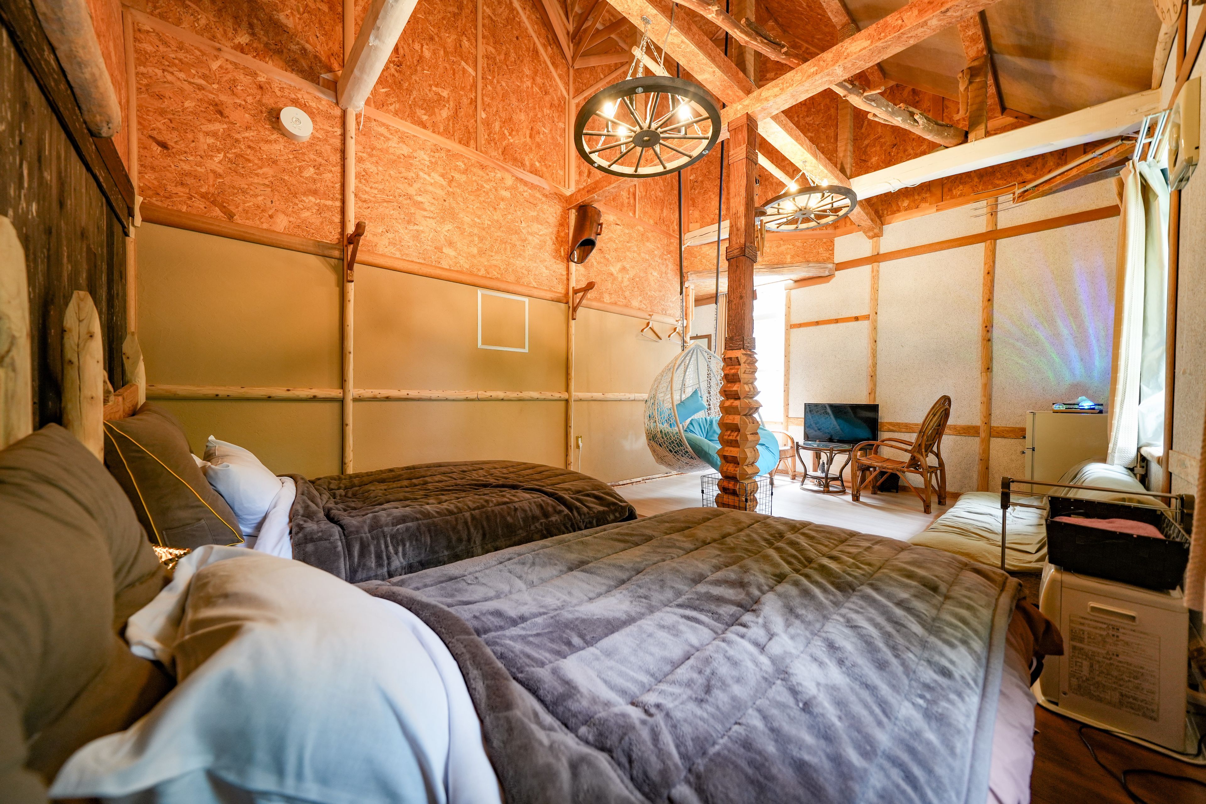 A rustic room with exposed wooden beams, a bed with a quilted duvet, a hanging chair, and a television.