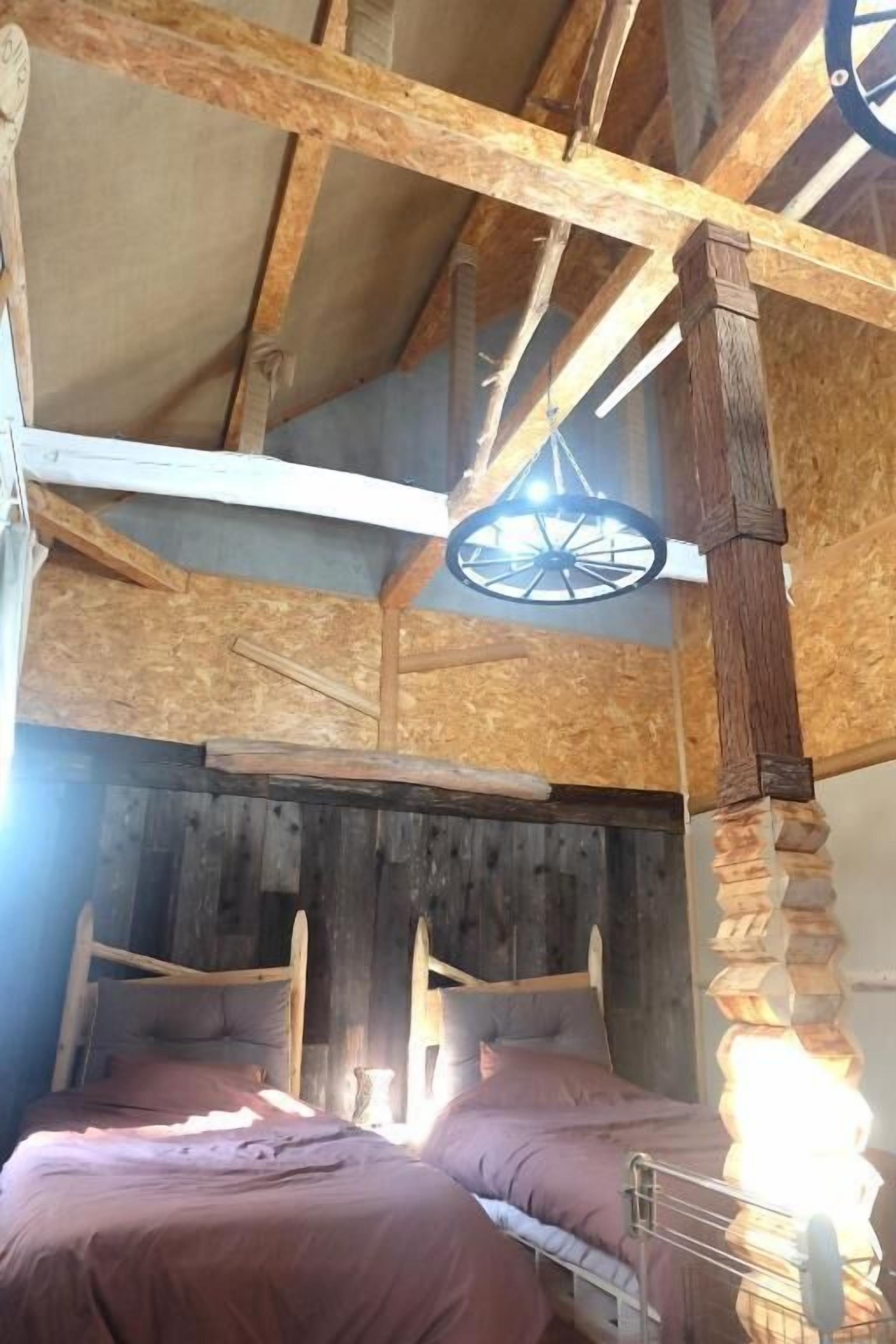 A rustic wooden room with two beds, a wooden ceiling, and a large wheel-like structure.