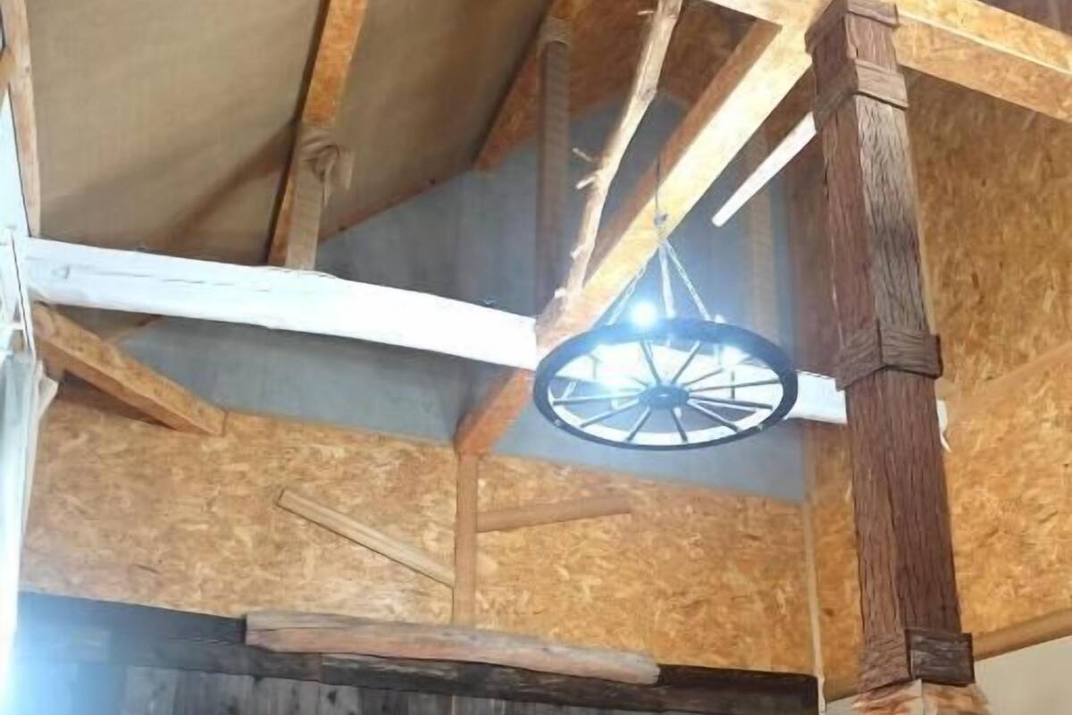 A rustic wooden room with two beds, a wooden ceiling, and a large wheel-like structure.